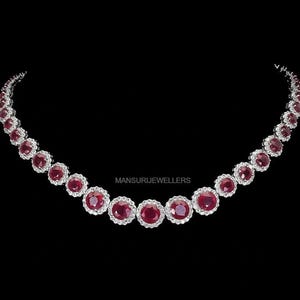 Op de afbeelding: Een elegante ketting met een reeks ronde, dieprode edelstenen, elk omringd door een halo van kleinere, sprankelende witte stenen. De ketting is geplaatst tegen een zwarte achtergrond, met de tekst "MANSURIJEWELLERS" zichtbaar.