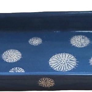 Puede incluir: Una fuente rectangular de cerámica azul con patrones florales blancos estilizados. Tiene dos asas con varillas doradas. El diseño general es una mezcla de estética moderna y rústica, adecuada para servir alimentos.