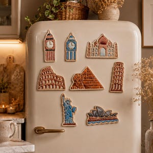 Peut inclure: Un ensemble d'aimants de réfrigérateur représentant des monuments célèbres tels que Big Ben, le Taj Mahal et la Tour de Pise. Les aimants sont fixés sur un réfrigérateur crème. Les motifs sont détaillés et colorés, offrant un élément décoratif.