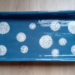 Pode incluir: Uma bandeja retangular de cerâmica azul com padrões florais brancos. A bandeja tem alças de bambu em cada extremidade. A bandeja tem aproximadamente 35 cm de comprimento e 18 cm de largura.