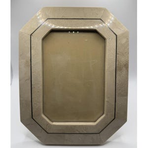 May include: An octagonal picture frame featuring a light beige, textured stone-like finish with a subtle marbled pattern. The frame includes a thin, dark, recessed border line that follows the inner and outer octagonal shape of the structure.