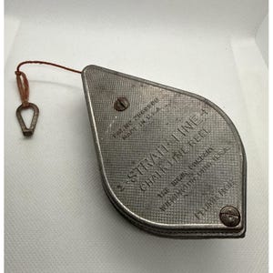 May include: A vintage silver-colored Strait-Line Chalk Line Reel Plumb Bob. The tool has a textured surface and features the text "Strait-Line Chalk Line Reel" and "The Irwin Company Wilmington, Ohio U.S.A." The reel is made in the U.S.A.