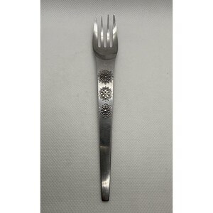 May include: A stainless steel fork with three tines and a long handle. The handle is decorated with three circular, ornate designs. The fork is designed for eating and is likely part of a set of silverware.