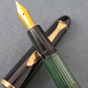 以下が含まれることがあります： 白のセラミックマグカップ、黒いハンドル、手書き風の「But first, coffee」の文字。マグカップは白い表面に置かれています。マグカップの高さは10cmです。