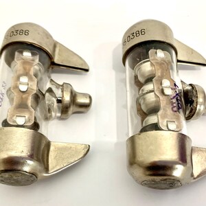 Puede incluir: Dos componentes el&eacute;ctricos vintage con tubos de vidrio transparente y tapas met&aacute;licas. Cada componente tiene un dise&ntilde;o &uacute;nico con elementos internos visibles a trav&eacute;s del vidrio. La parte superior de cada componente est&aacute; marcada con el n&uacute;mero "60386".