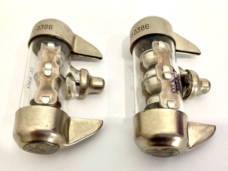 Puede incluir: Dos componentes el&eacute;ctricos vintage con tubos de vidrio transparente y tapas met&aacute;licas. Cada componente tiene un dise&ntilde;o &uacute;nico con elementos internos visibles a trav&eacute;s del vidrio. La parte superior de cada componente est&aacute; marcada con el n&uacute;mero "60386".