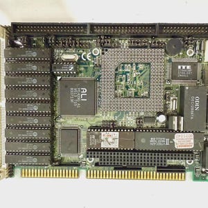 Puede incluir: Una placa de circuito verde con varios componentes electrónicos, incluyendo chips y conectores. La placa tiene una unidad central de procesamiento y varias ranuras y puertos. La placa tiene el texto "ALI" y "ODIN" impreso.