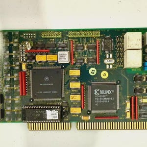 May include: A green circuit board with various electronic components, including chips, resistors, and connectors. The board features text and labels, with gold-colored pins along the bottom edge. A black connector is on the right side.