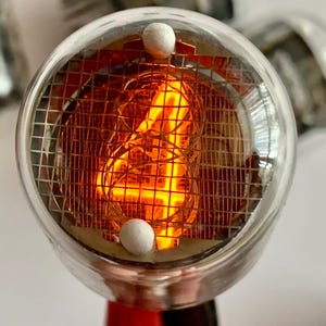 May include: Close-up of a vintage Nixie tube with a glowing orange number eight. The tube is encased in clear glass with a metal mesh and two white spherical components. The base is red and black.