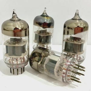 Puede incluir: Un conjunto de válvulas de vacío vintage. Los tubos de vidrio tienen una parte superior plateada y un cuerpo transparente, que revela los componentes internos. Los tubos tienen múltiples pines en la base. Un tubo está acostado de lado.