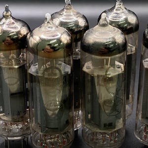 Peut inclure: Une collection de tubes à vide en verre transparent avec des composants métalliques internes et des sommets argentés. Chaque tube cylindrique possède une pointe en verre au sommet et des broches métalliques à la base, avec des structures internes visibles.