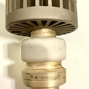 Può includere: Una valvola termoionica elettronica vintage con una parte superiore argentata alettata, una sezione centrale in ceramica bianca e una base metallica. La base presenta marchiature impresse, tra cui "ГИ-39Б 8812". Il tubo è progettato per applicazioni elettroniche.