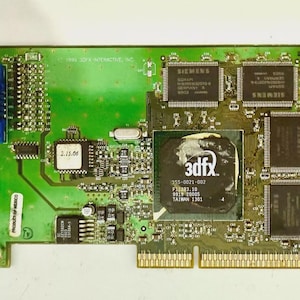 May include: A green circuit board with various electronic components, including chips labeled "SIEMENS" and a central chip with "3dfx" branding. It has a blue connector and gold-colored pins.