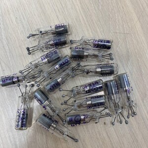 Puede incluir: Una colección de pequeños tubos de vidrio transparente con componentes metálicos y cables negros. Los tubos tienen texto morado que dice "MTX-90", "MTX-190" y "OTK". Los objetos están dispersos sobre una superficie de madera clara.