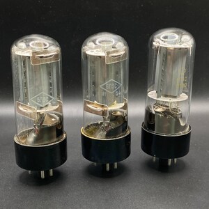 May include: Three cylindrical vacuum tubes with clear glass envelopes and black circular bases. Each tube features internal metal components and a diamond-shaped logo with the Cyrillic text 6P3S printed on the glass surface, along with VI 64 markings.