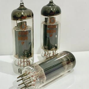 May include: Three vintage vacuum tubes with clear glass bodies and dark gray tops. Each tube has a series of pins at the base and internal components visible through the glass. The tubes have the text "6041" and "SB04" printed on them.
