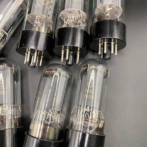 Może przedstawiać: Kolekcja szklanych lamp próżniowych z czarnymi okrągłymi podstawami i metalowymi pinami. Każda lampa posiada wewnętrzne szare metalowe elementy oraz nadrukowany tekst, w tym 6P3C i 0582, widoczny przez przezroczystą szklaną obudowę.