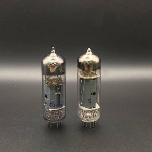 Könnte beinhalten: Zwei zylindrische Glas-Vakuumröhren mit internen Metallkomponenten und Stiften an der Basis. Die linke Röhre zeigt den blauen Schriftzug "OTK 5" und die rechte Röhre hat eine blaue "5" auf der internen grauen Metallstruktur aufgedruckt.