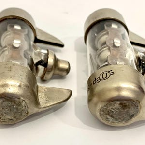 Puede incluir: Dos v&aacute;lvulas de vac&iacute;o vintage, con bases de metal plateado y cilindros de vidrio transparente. Cada v&aacute;lvula tiene una base redondeada, un cuerpo cil&iacute;ndrico de vidrio y una tapa superior. El texto "OEP-5" es visible.