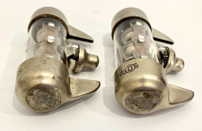 Puede incluir: Dos v&aacute;lvulas de vac&iacute;o vintage, con bases de metal plateado y cilindros de vidrio transparente. Cada v&aacute;lvula tiene una base redondeada, un cuerpo cil&iacute;ndrico de vidrio y una tapa superior. El texto "OEP-5" es visible.