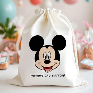 May include: Off-white drawstring bag featuring a smiling Mickey Mouse face in black, red, and tan. The text "MARTIN'S 2ND BIRTHDAY" is printed in black below the character. The bag is likely for a child's birthday party.