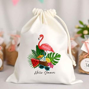 May include: A white drawstring bag featuring a pink flamingo, watermelon, sunglasses, and tropical leaves. The words "Hello Summer" are printed below the graphic. The bag is tied at the top with a white drawstring.