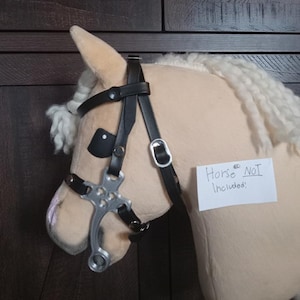 May include: A tan plush horse head with a black leather bridle and silver-colored bit. The horse has a white mane and a paper sign that reads "Horse NOT Included!"