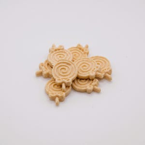 May include: A pile of light brown, lollipop-shaped cookies with a spiral design. Each cookie has a small stick and a decorative top. The cookies are arranged on a white surface.