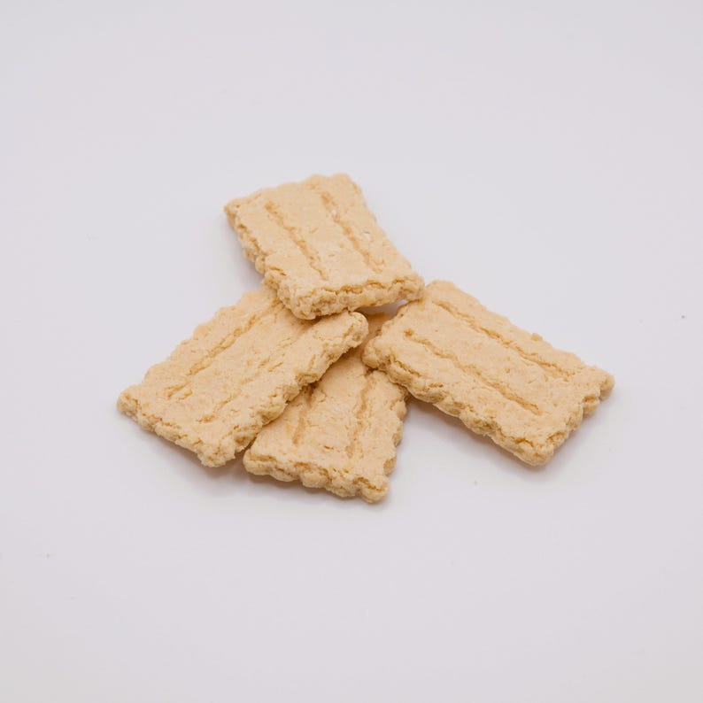 May include: A pile of five rectangular, light tan crackers with a ridged texture. The crackers have a slightly uneven, textured surface and are arranged on a white background. The edges of the crackers are also textured.