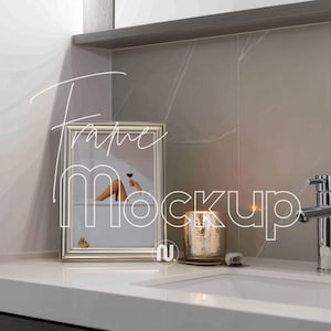 Puede incluir: Un marco plateado con una impresión artística que muestra a una persona en una bañera con una copa de vino. Un portavelas dorado y un lavabo están en primer plano. El texto "Frame Mockup" es visible.