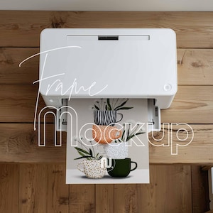 May include: A white printer is printing a design featuring stacked coffee cups with floral arrangements. The cups are in various colors and patterns, including stripes, polka dots, and a speckled design. The words "Frame Mockup" are written on the image.