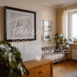 May include: A black framed picture with a floral design hangs on a beige wall. The words "Frame Mockup" are written in white script across the image. A wooden chest of drawers is in the foreground.