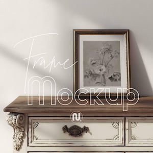 May include: A framed floral print with a gold-colored frame rests on a wooden surface. The frame is rectangular and contains a black and white floral illustration. The frame is placed on a white and brown antique dresser. The text "Frame Mockup" is written on the image.