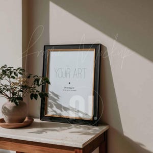 May include: A black framed art print with gold trim, displaying the text "YOUR ART". The frame is propped on a marble-topped table next to a vase with greenery. The print size is 40 x 50 cm.