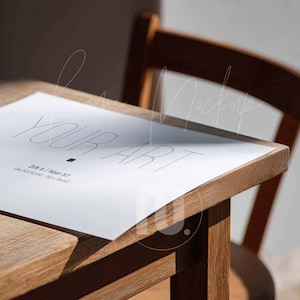 Peut inclure: Une feuille de papier blanche avec l'inscription "YOUR ART" dans une police minimaliste, posée sur une table en bois. Le papier contient également le texte "DIN A / Neary 57 (A4/A3/A2/A1 - 50 x 70cm)". Une chaise en bois est en arrière-plan.