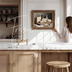 May include: A framed painting of cheese, a knife, and a pepper grinder. The painting has a gold ornate frame. The image is in a kitchen setting with a marble countertop and wooden cabinets. The text "Frame Mockup" is overlaid on the image.