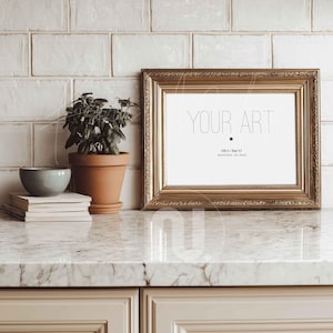 以下が含まれることがあります： 白い背景に「YOUR ART」の文字が入った金色の長方形のフォトフレーム。小さな鉢植え、本の山、青いボウルが大理石のカウンタートップに置かれています。フレームは30 x 70cmです。