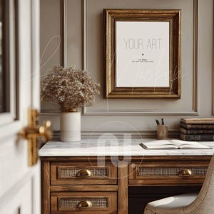 以下が含まれることがあります： 「YOUR ART」の文字が入った金色の額縁のアートワークが灰色の壁に掛けられています。 大理石の天板の木製デスクとドライフラワーの花瓶が前景にあります。 デスクには真鍮製の取っ手が付いた引き出しがあります。