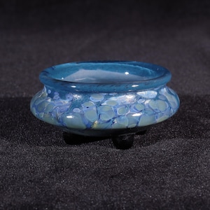 Może przedstawiać: Mała, niebiesko-zielona szklana miska z wzorami w kropki. Miska ma trzy małe nóżki i stoi na czarnym tle.