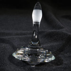 May include: A clear glass spinning top with a white frosted top and a silver base.