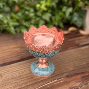 May include: A decorative copper bowl with a turquoise base and rim. The bowl has a scalloped edge and a hammered interior. The bowl is sitting on a wooden surface.