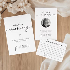 以下が含まれることがあります： 「Share a memory」の文字が書かれた白いカード。1枚には男性の写真、もう1枚には書き込み用の線があります。これらのカードは、思い出を共有するために使用されます。