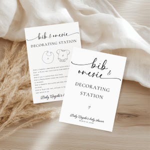 May include: Two white cards with black text that read "bib & onesie DECORATING STATION". One card has instructions and illustrations of a bib and onesie. The other card says "Baby Angelo's baby shower MARCH 16, 2030".