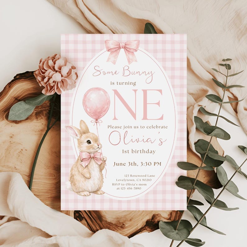 Op de afbeelding: Een roze en wit geruit uitnodigingskaart met de tekst "Some Bunny is turning ONE". De kaart toont een aquarel illustratie van een konijn met een ballon en een roze strik. De uitnodiging is voor Olivia's 1e verjaardag.