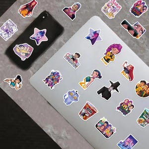 May include: A collection of colorful stickers featuring cartoon characters and designs. Stickers are placed on a laptop and a smartphone. Designs include a star, a cat, and characters with the names "Rumi", "Mira", and "Zoey".
