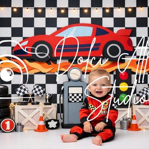 May include: A baby in a red and black racing suit smiles in front of a race car-themed backdrop. The scene includes a red race car cutout, tires, checkered flags, and a gas pump prop. The backdrop has a black and white checkered pattern.
