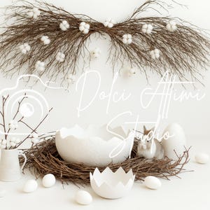 Könnte beinhalten: Eine Osterdekoration mit einem Nest aus Zweigen, weißen Eiern und einer kleinen Hasenfigur. Ein großer Ast mit Baumwollakzenten hängt darüber. Eine weiße Vase mit Zweigen und Baumwollblüten befindet sich links.