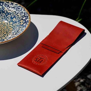 May include: A red leather bill holder with the embossed text "514 RESTAURANT BAR" on a white table. A decorative blue and white patterned bowl is in the background.