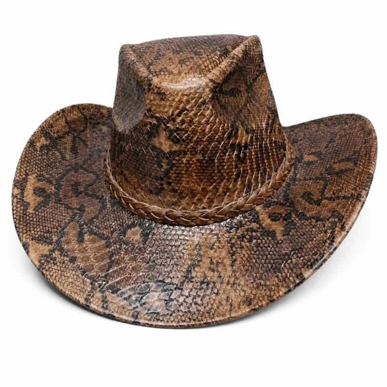 May include: A brown and black cowboy hat featuring a detailed snakeskin pattern across the entire surface. The hat includes a braided band encircling the base of the crown and a wide, curved brim that slopes downward on both sides.