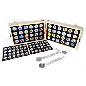 Puede incluir: Una caja de madera con tapa abatible, que contiene una colección de botones magnéticos redondos de colores. La caja está abierta, mostrando los botones dispuestos en filas. También se incluyen dos collares de plata con colgantes magnéticos.